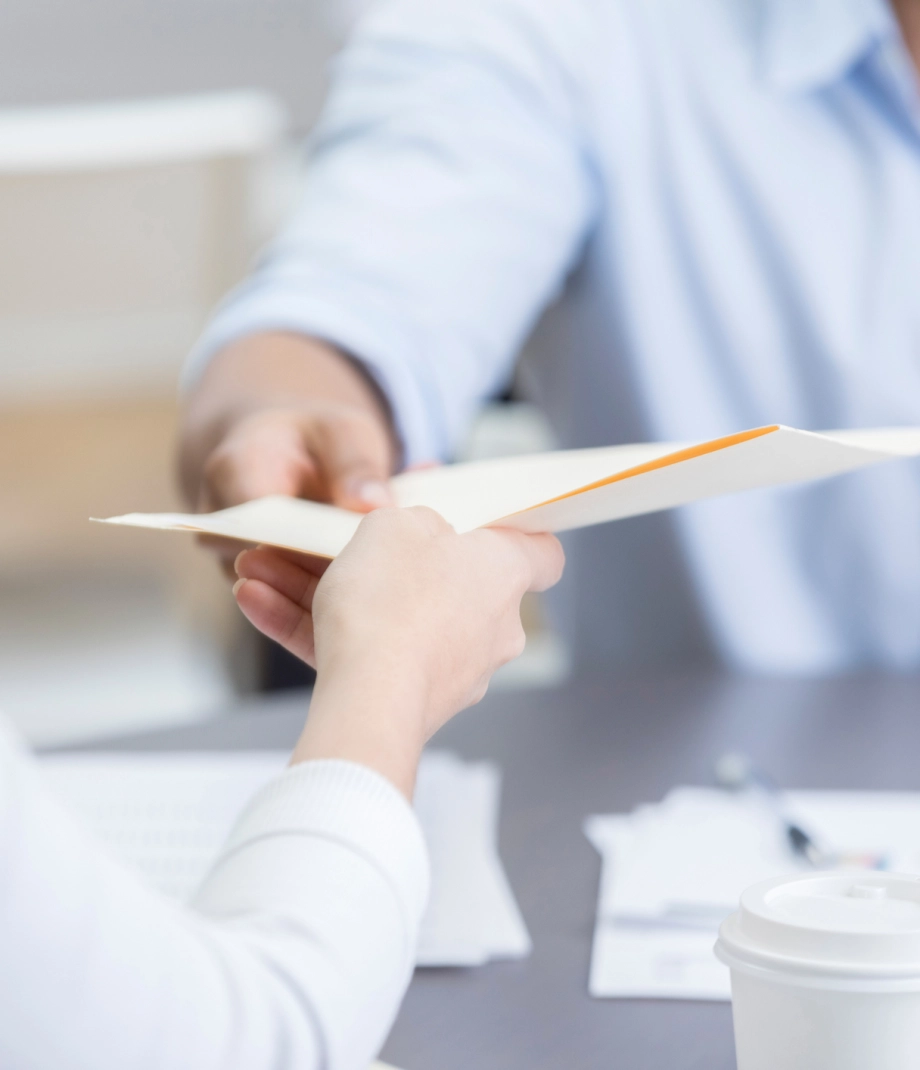 Closeup of two coworkers passing folder across table